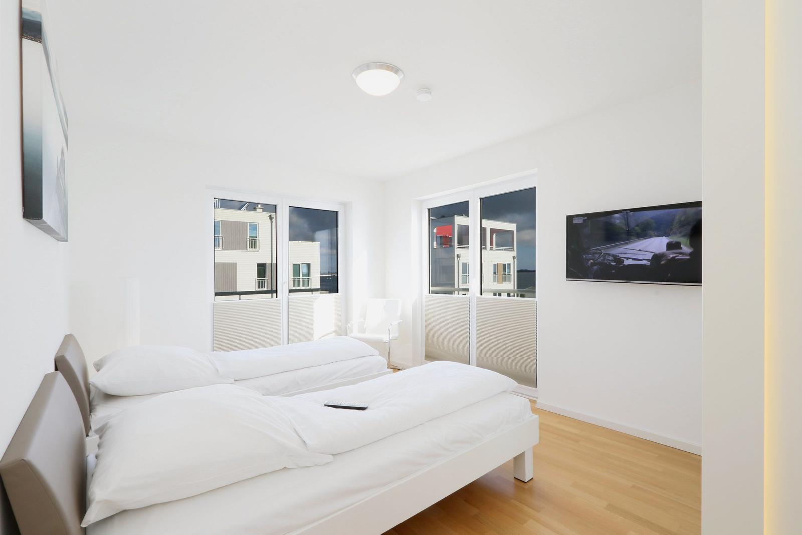 Schlafzimmer mit Bett, TV und Fenstern zum Balkon.