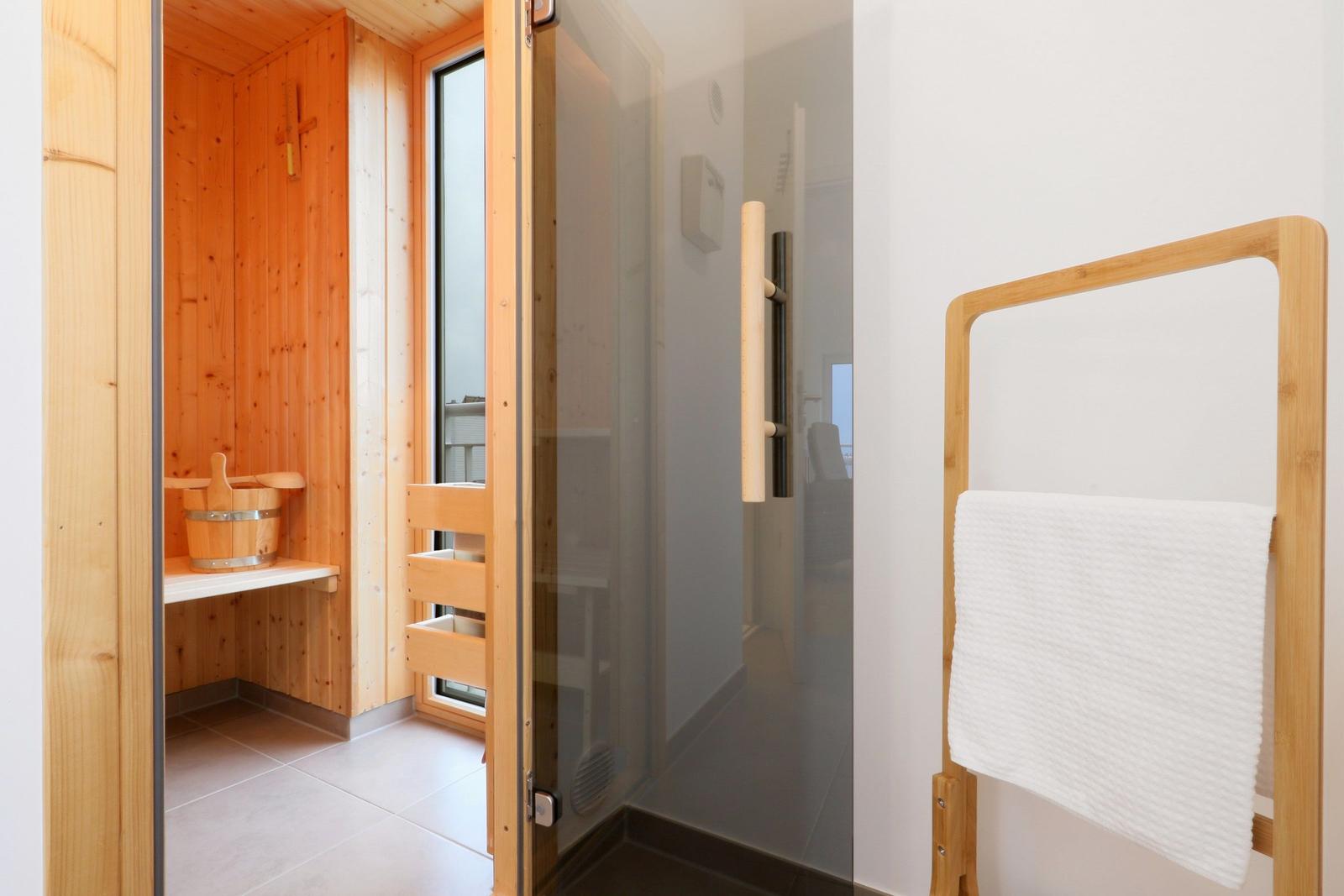 Sauna mit Holzwand und Einstiegstür. Weiße Wand und Handtuchhalter daneben.