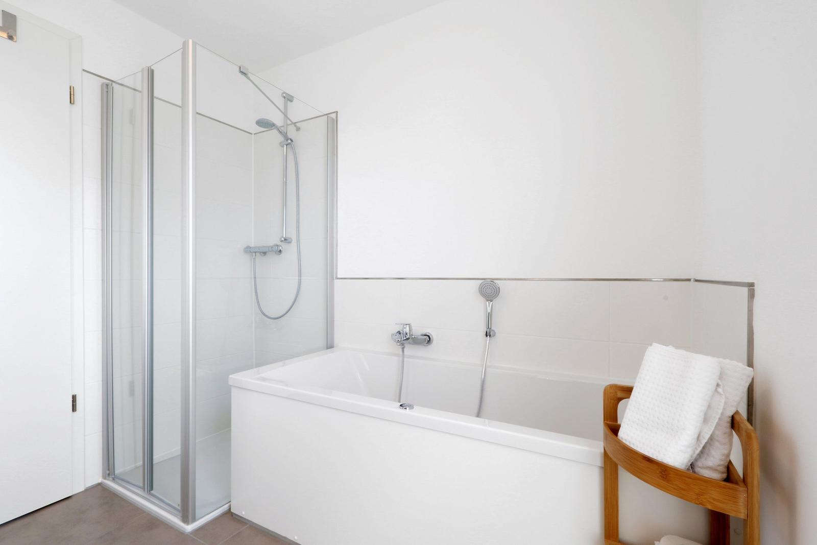 Badezimmer mit Dusche und Badewanne, daneben Holzregal mit Handtüchern.