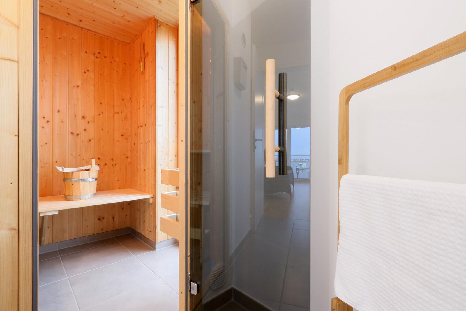 Sauna mit Holzwand und Sitzbank. Dampfdusche und Handtuchhalter sind sichtbar.