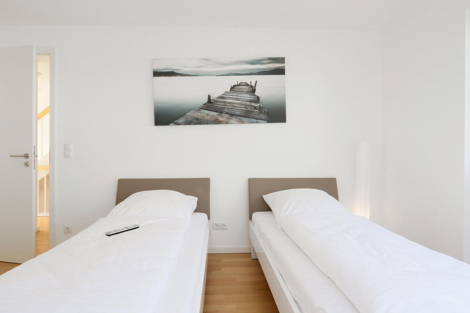 Zwei Einzelbetten mit weißer Bettwäsche und Wandbild mit Steg.