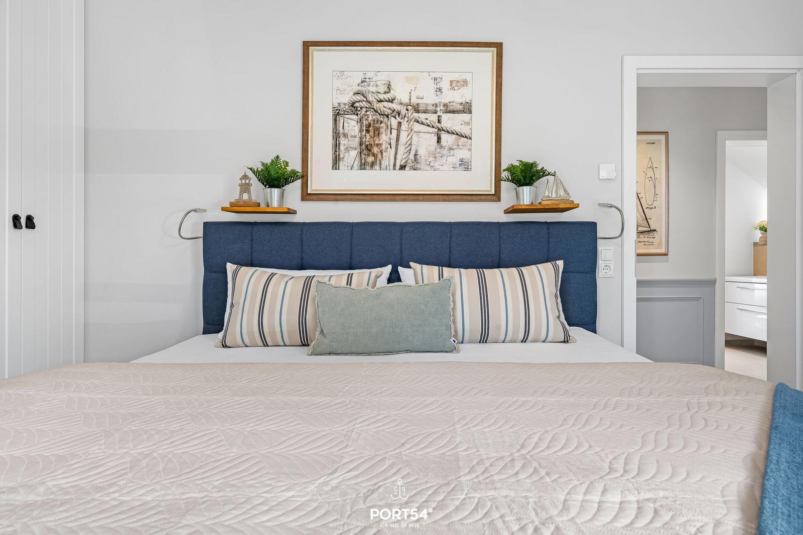 Schlafzimmer mit blauem Kopfteil, gestreiften Kissen und Wandbild mit Seil.