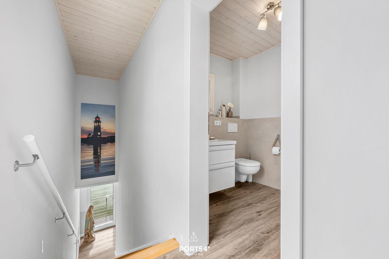 Badezimmer mit Toilette und Waschbecken. Flur mit Leiter und Bild eines Leuchtturms.