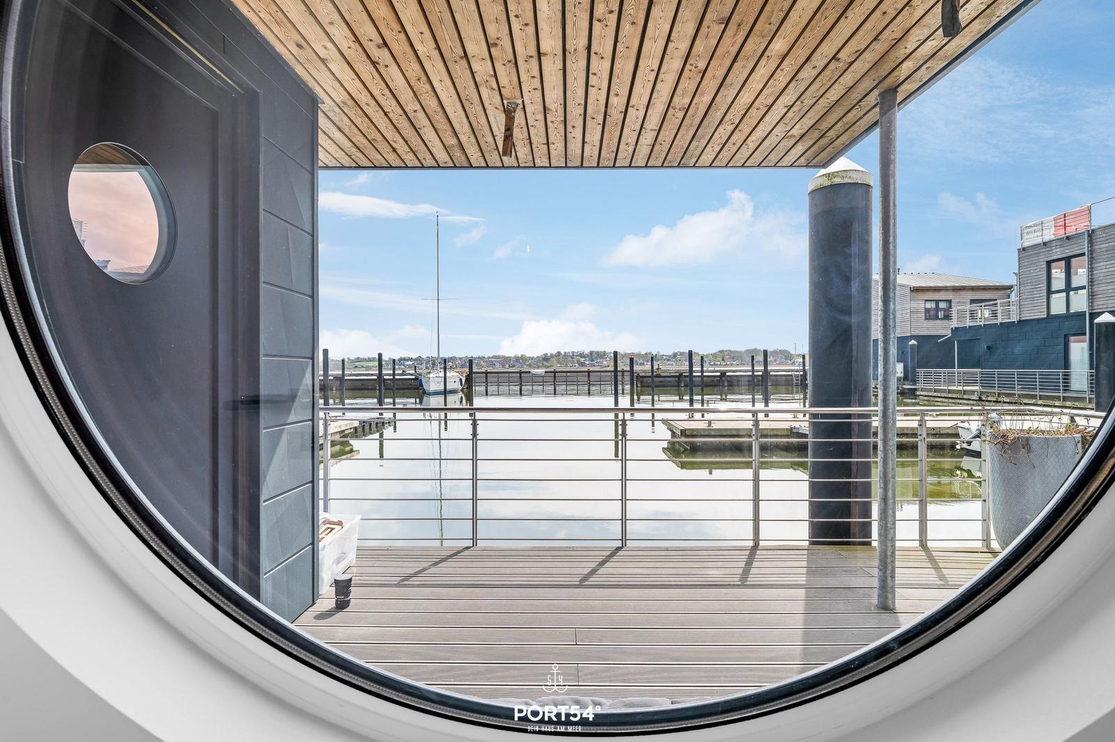 Durch runde Fensterblick auf Hafen mit Booten und modernen Gebäuden.