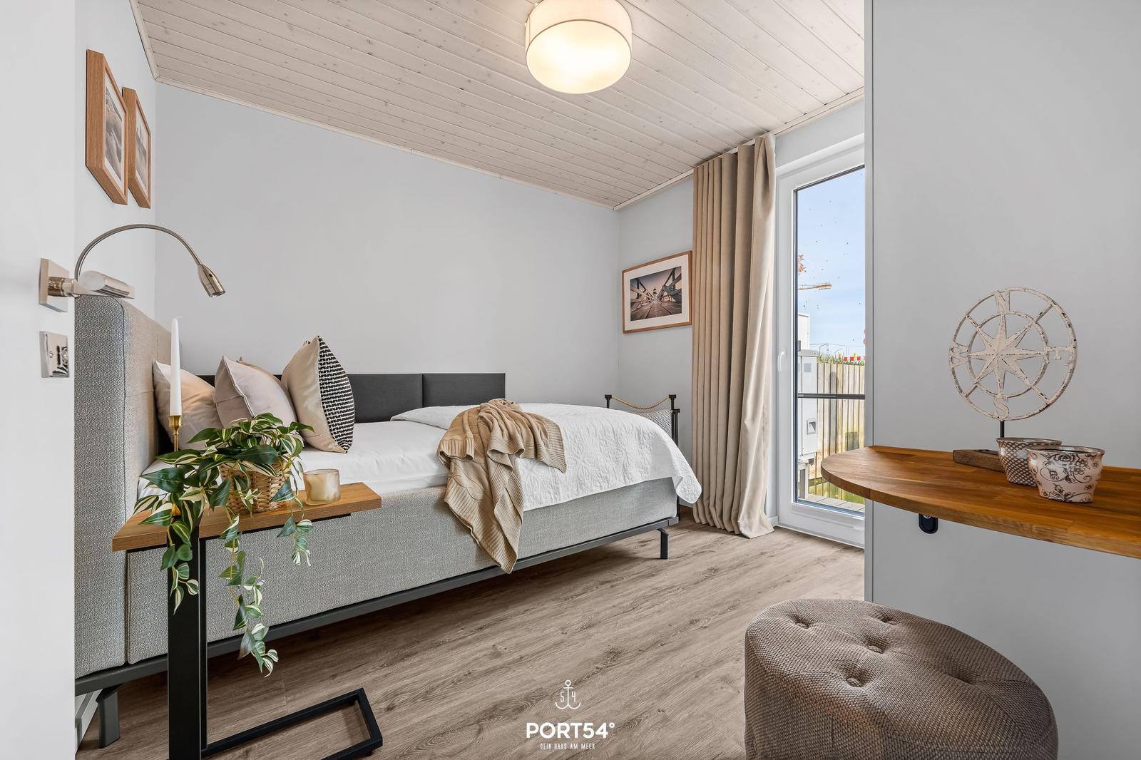 Schlafzimmer mit Bett, Schreibtisch und Fenster. Holzfußboden und weiße Wände.