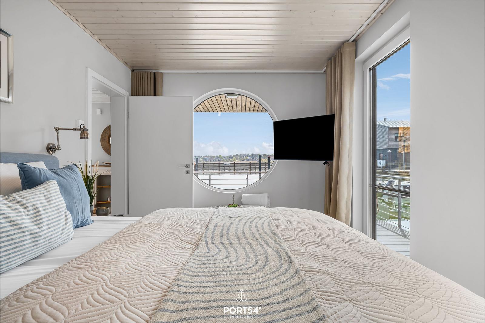 Schlafzimmer mit runder Aussichtöffnung und Balkon. Bett mit gesteppter Decke.