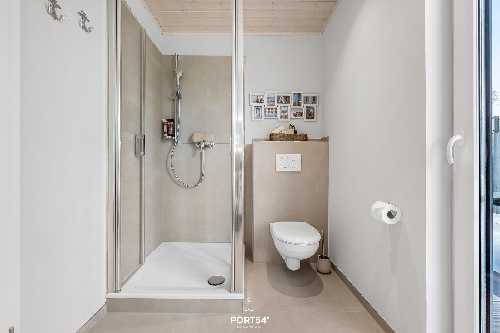 Duschbereich mit Toilette und Wandbildern. Moderne Einrichtung mit Glaswand.