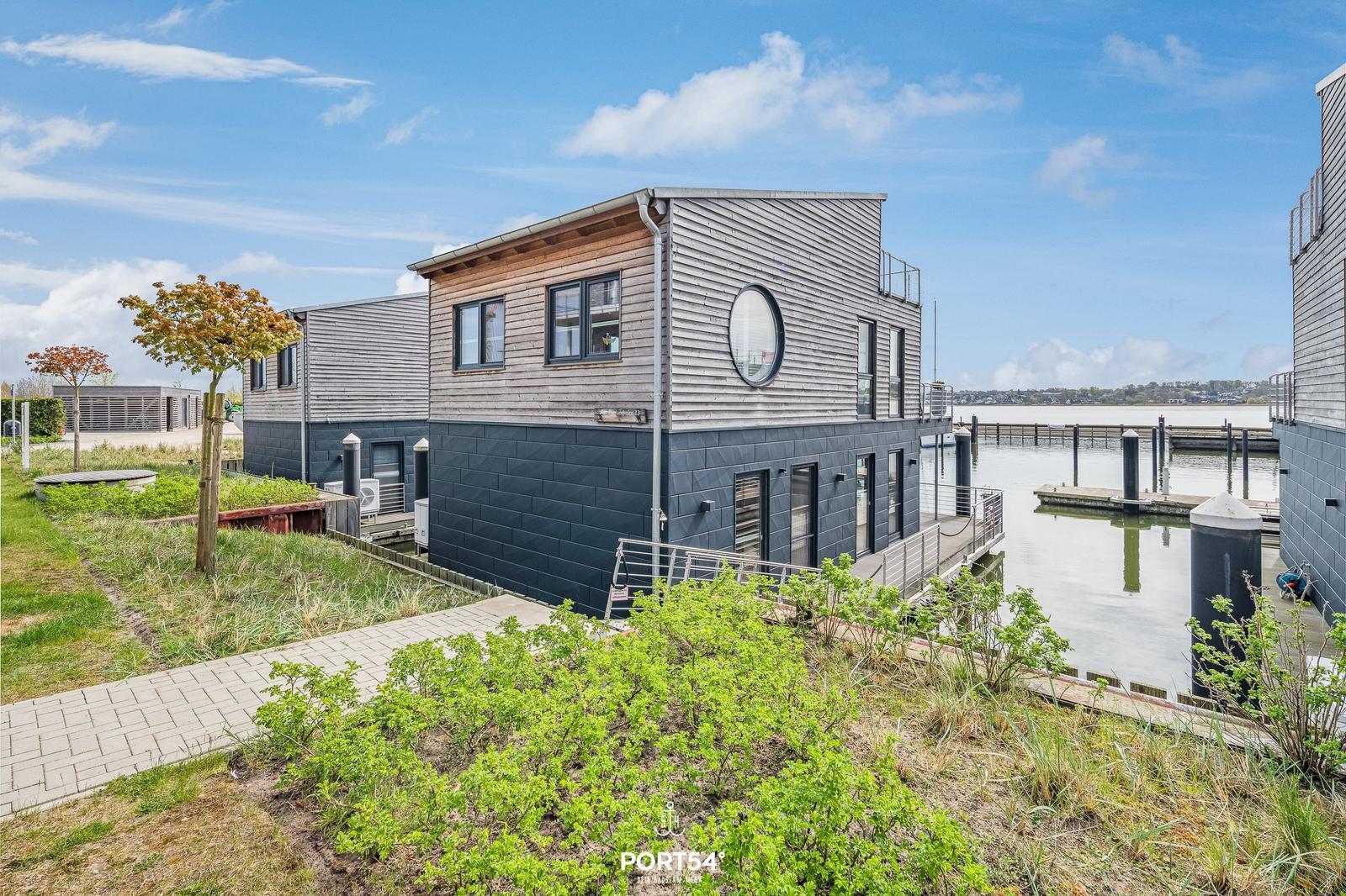 Moderne Hausanlage am Wasser mit Holzfassade und runden Fenster.