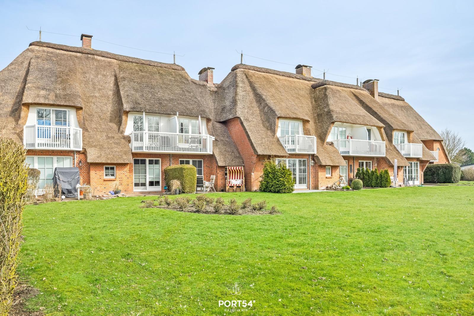 Ferienhaus mit Strohdach und Balkonen auf grünem Grundstück