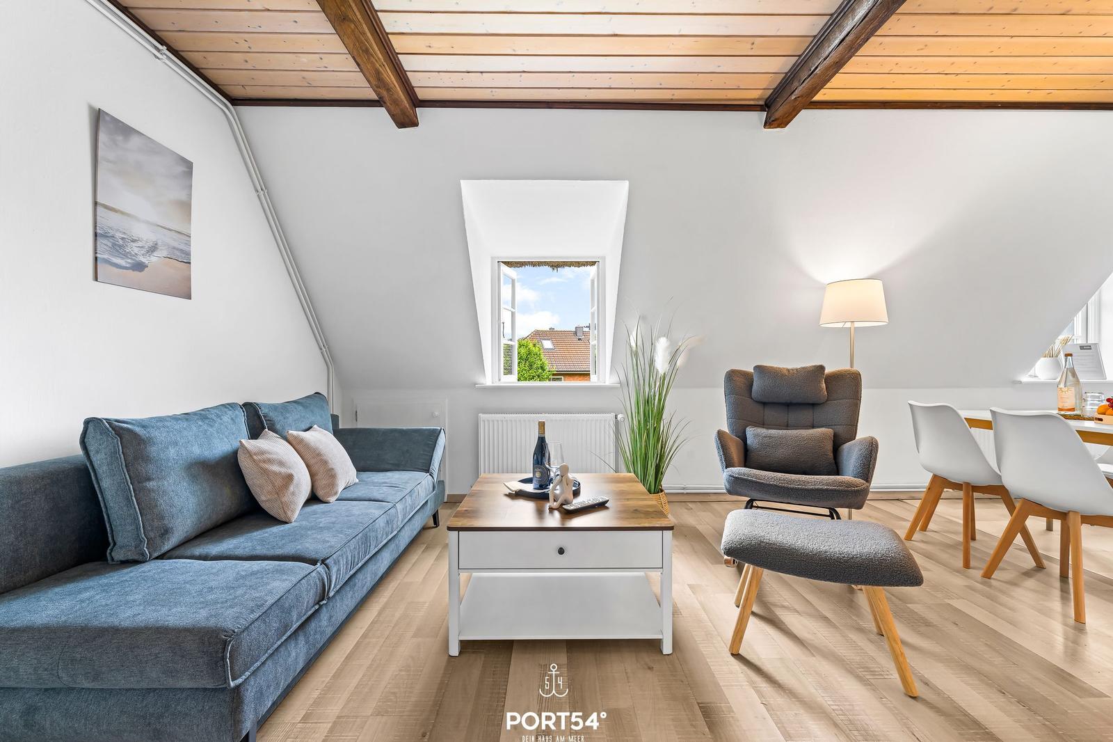 Wohn- und Essbereich mit Sofa, Sessel und Holzboden unter Holzdecke.
