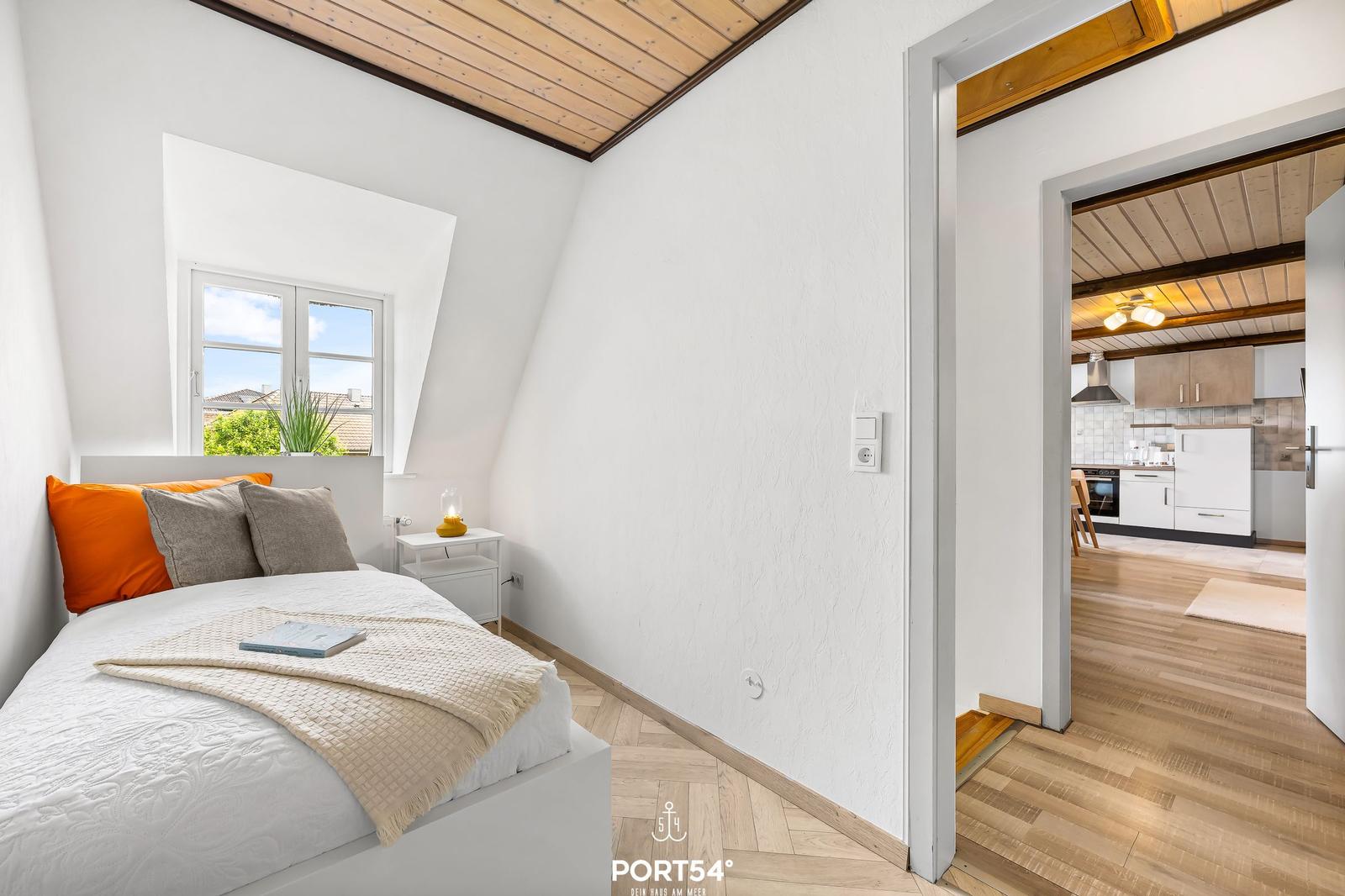 Schlafzimmer mit Bett, Fenster und Blick in die Küche.