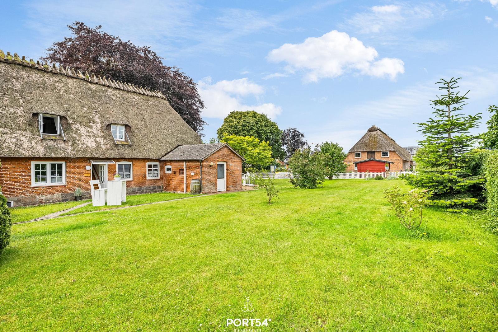 Haus mit Strohdach, großer Garten und weiteres Gebäude im Hintergrund.