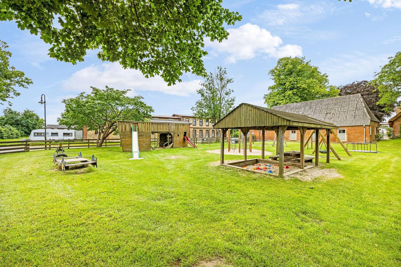 Großer grüner Garten mit Spielplatz, Sandkasten und Holzspielgeräten.