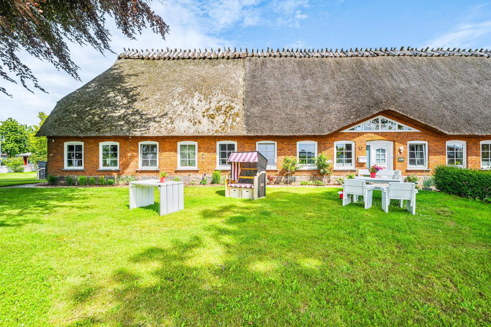 Haus mit Strohdach, weißer Gartenmöbel und grünem Rasen.