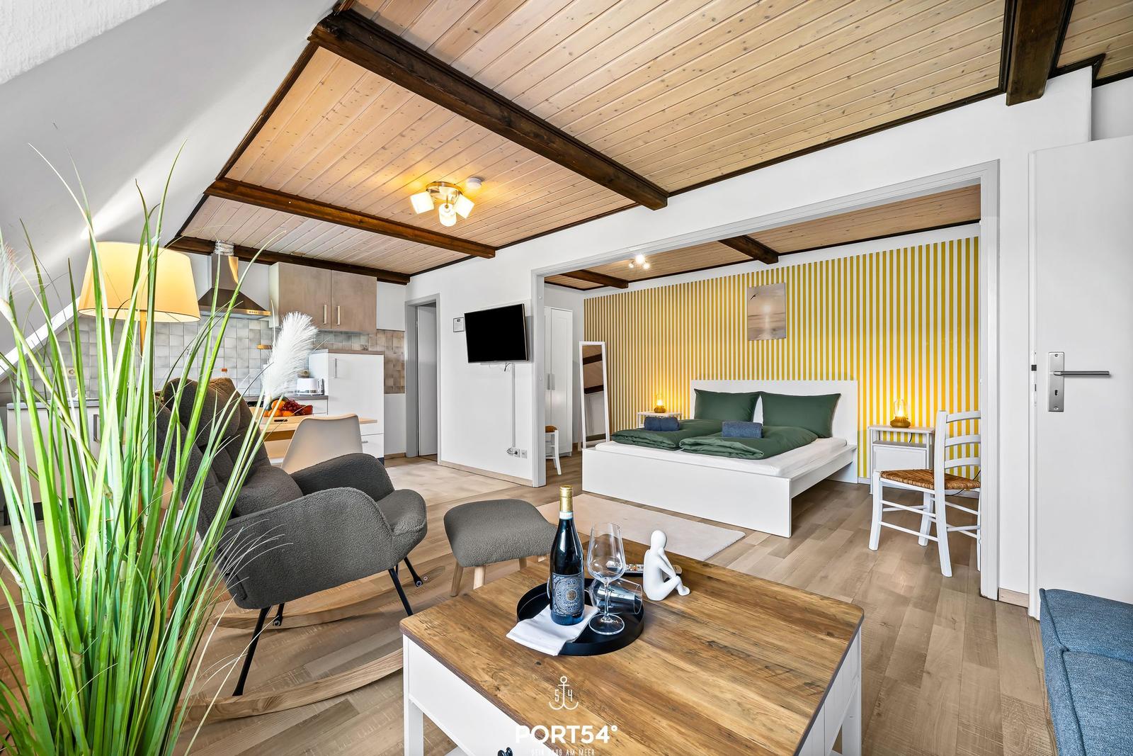 Wohnbereich mit Schlafzimmer, Küche und Holzdecke. Möbel und Dekoration sichtbar.