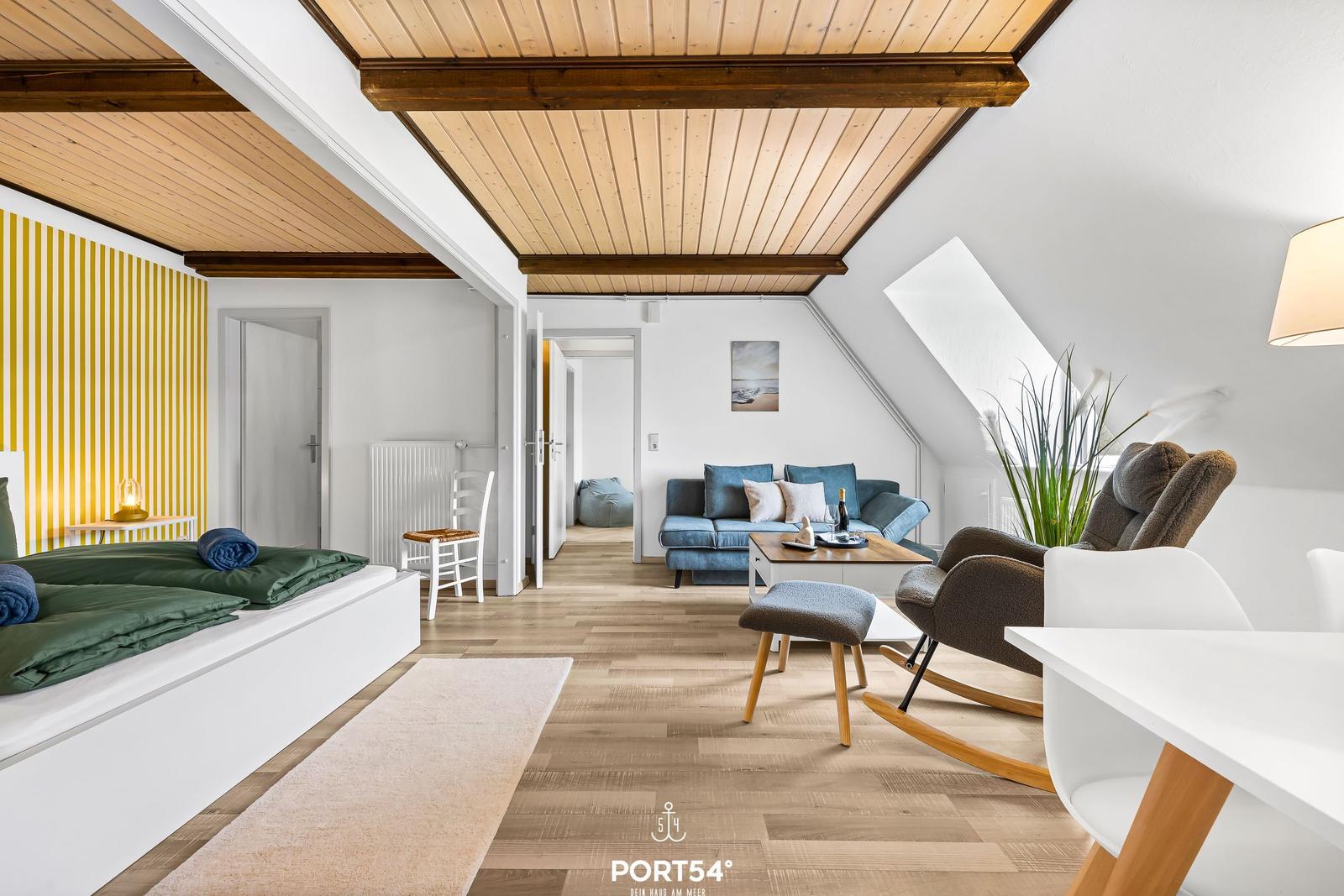 Wohnbereich mit Sofa, Sessel und Schlafplatz unter Holzdecke