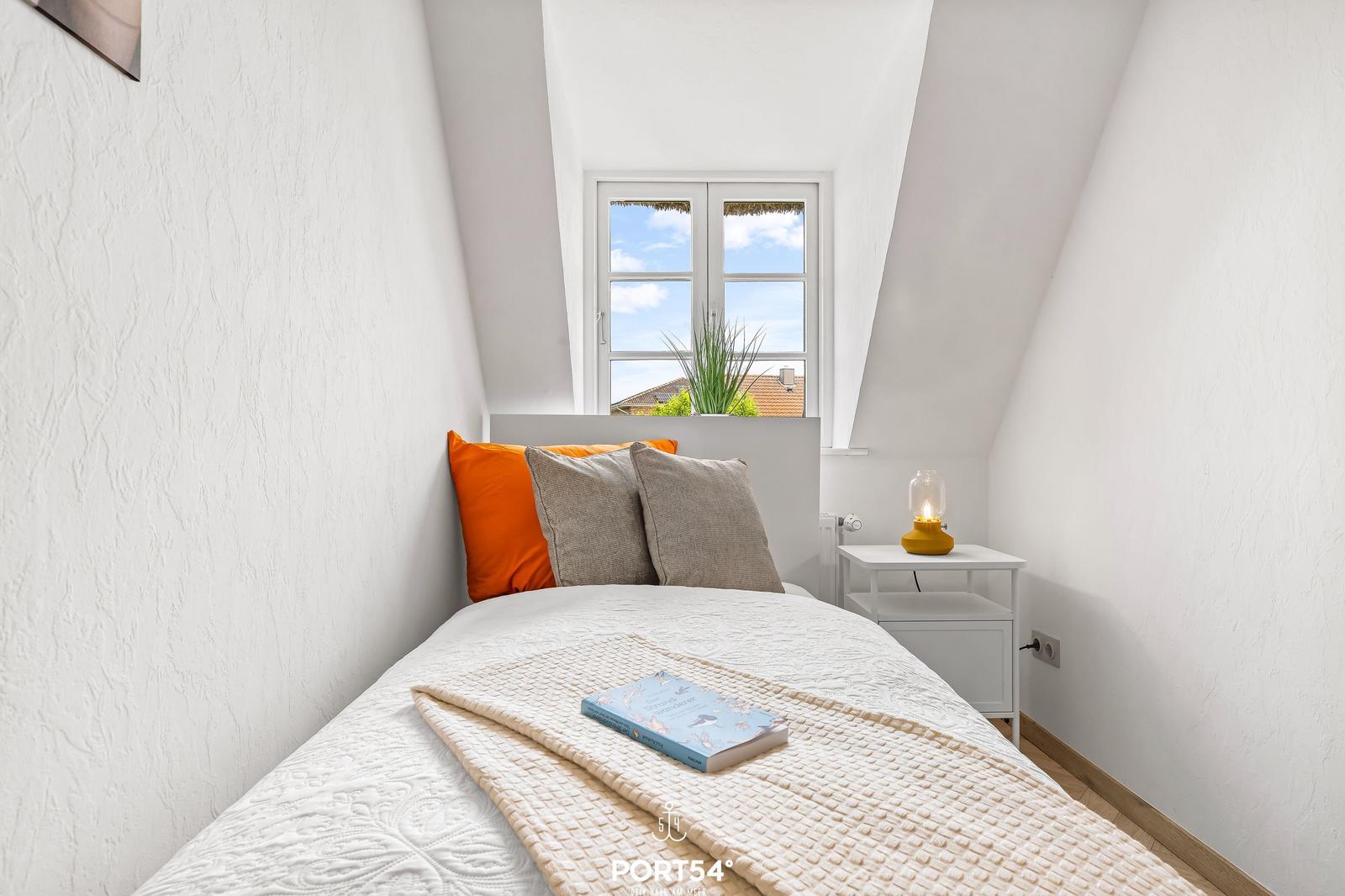 Schlafzimmer mit Dachschrägen, Fenster, Bett und Nachttisch.