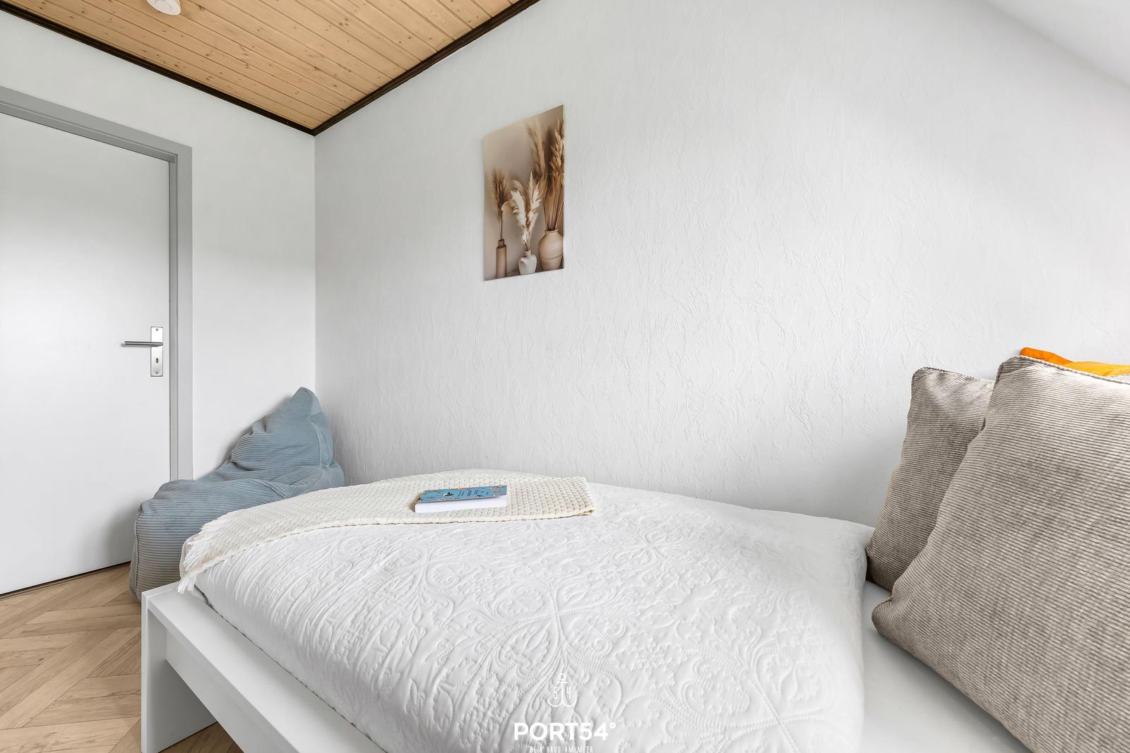 Schlafzimmer mit weißem Bett, Holzdecke und Wandbild.