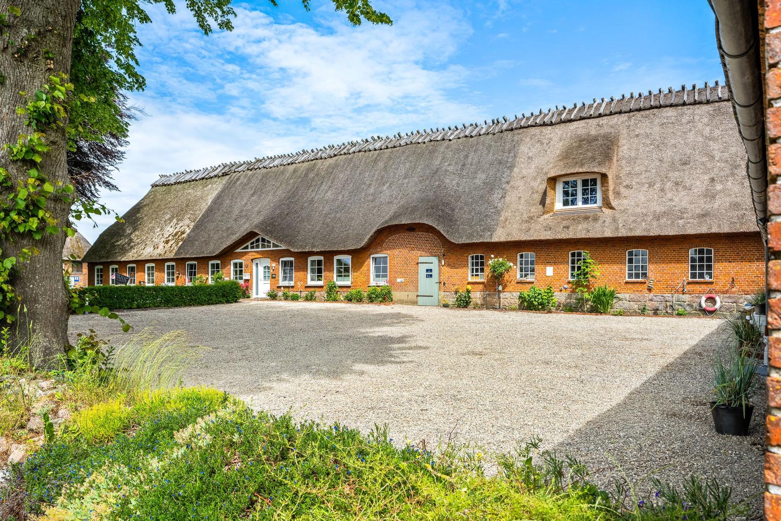 Haus mit Strohdach, Steinmauer und Grünanlagen im Vorgarten.