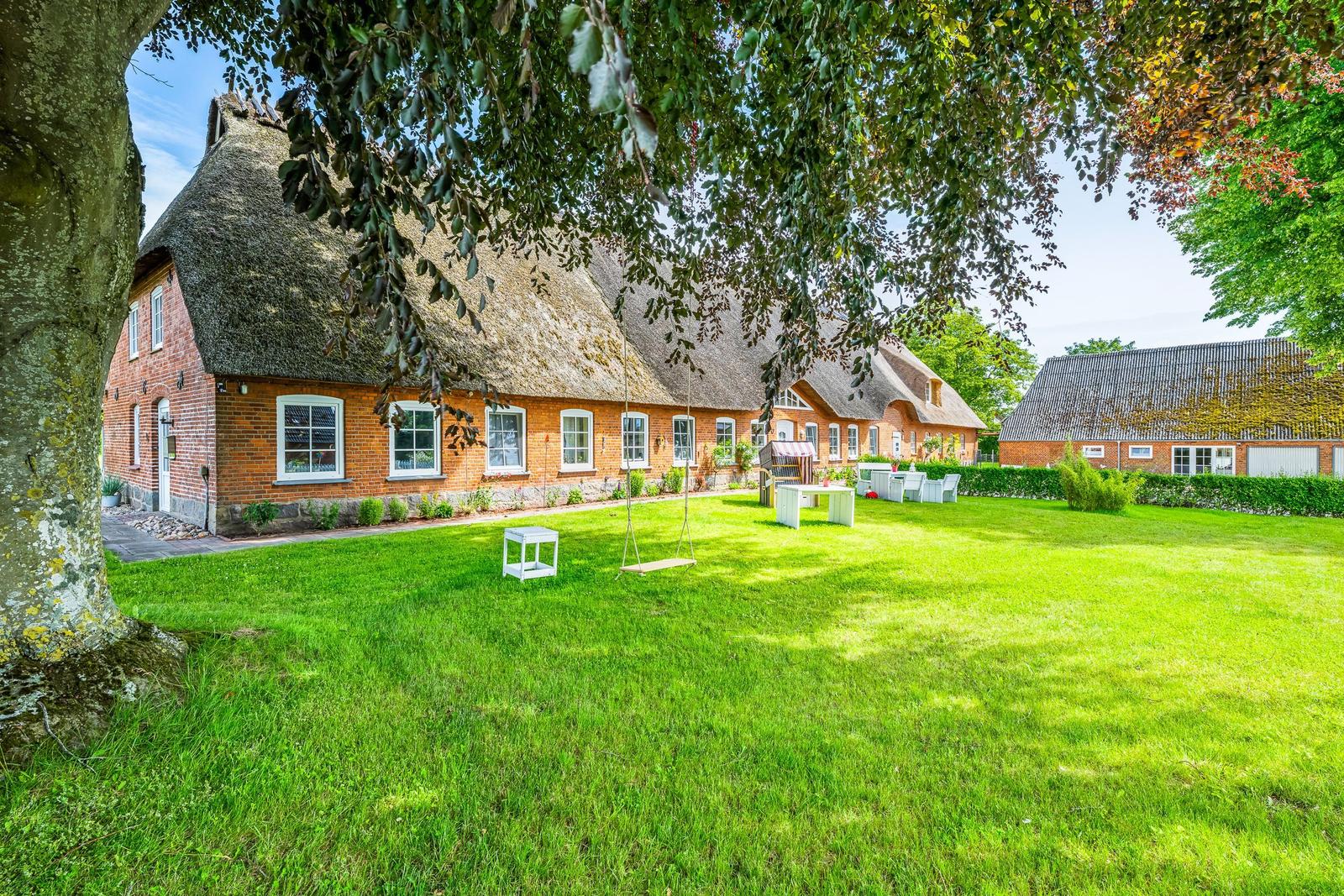 Roter Backsteinhaus mit Strohdach und großer grüner Garten mit Schaukel.