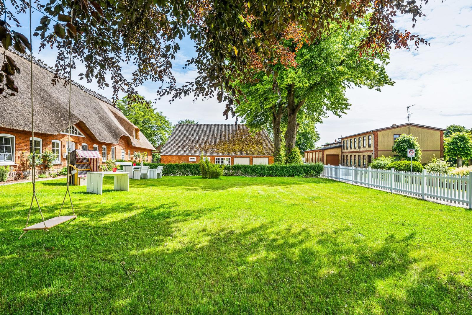 Haus mit Dach aus Stroh, großes Grasfeld, Schaukel und weißer Zaun.