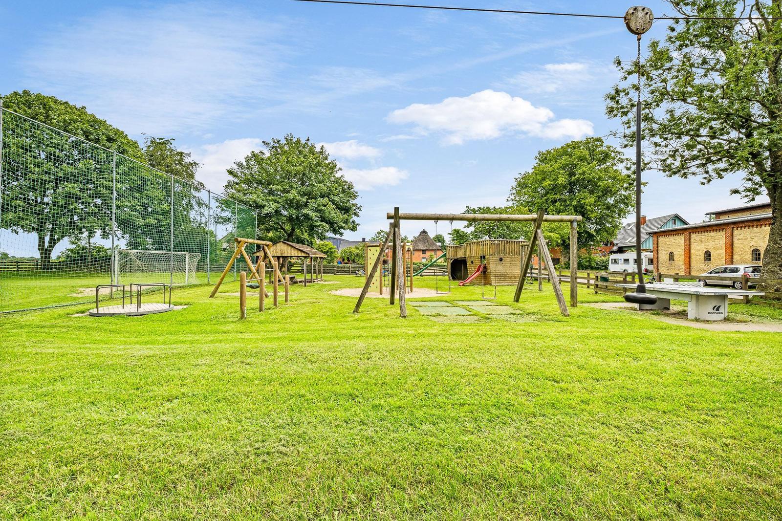 Großer grüner Spielplatz mit Holzspielgeräten, Sandkasten und Fußballtor.