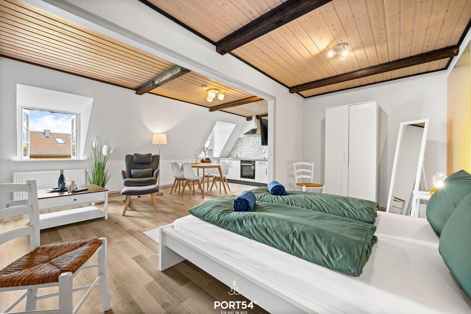 Schlafzimmer mit Doppelbett, Küche und Wohnbereich unter Holzdecke.