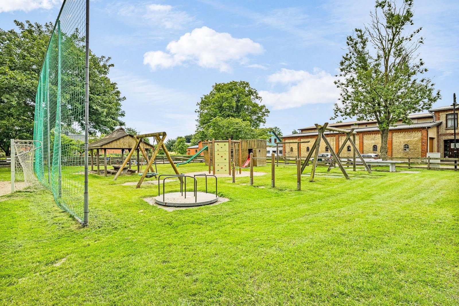 Großer Spielplatz mit Klettergerüst, Rutsche und Sandkasten auf grünem Rasen.