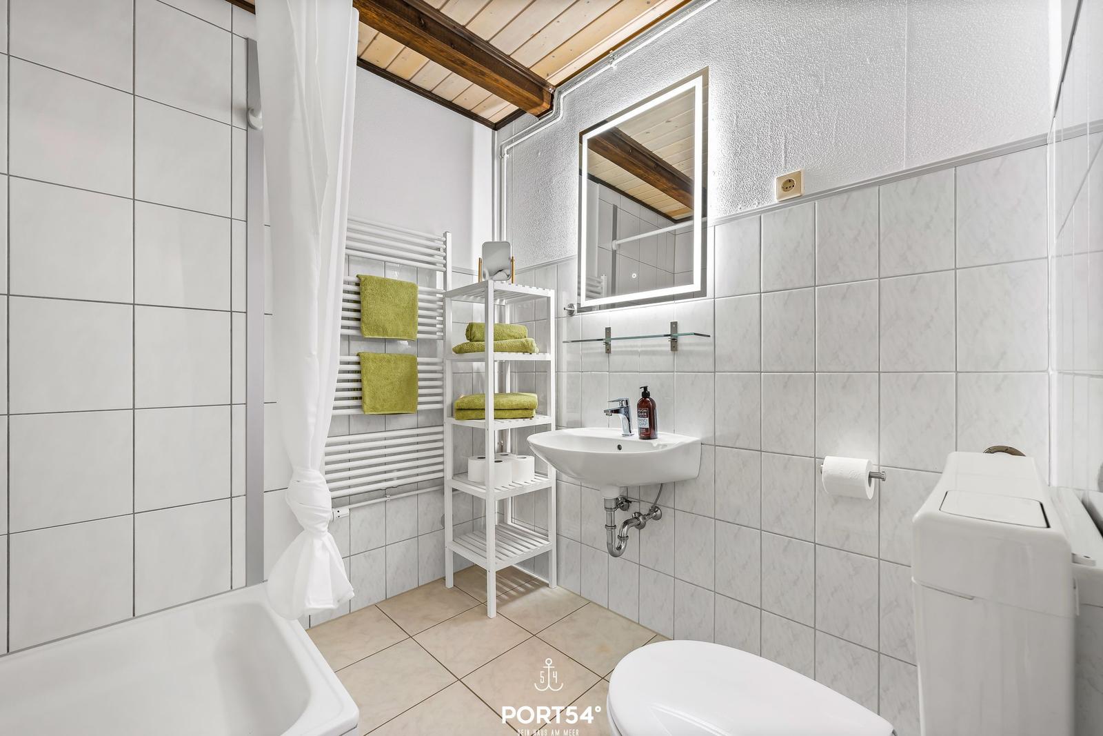 Badezimmer mit Dusche, Waschbecken und Toilette. Weiße Fliesen und grüne Handtücher.