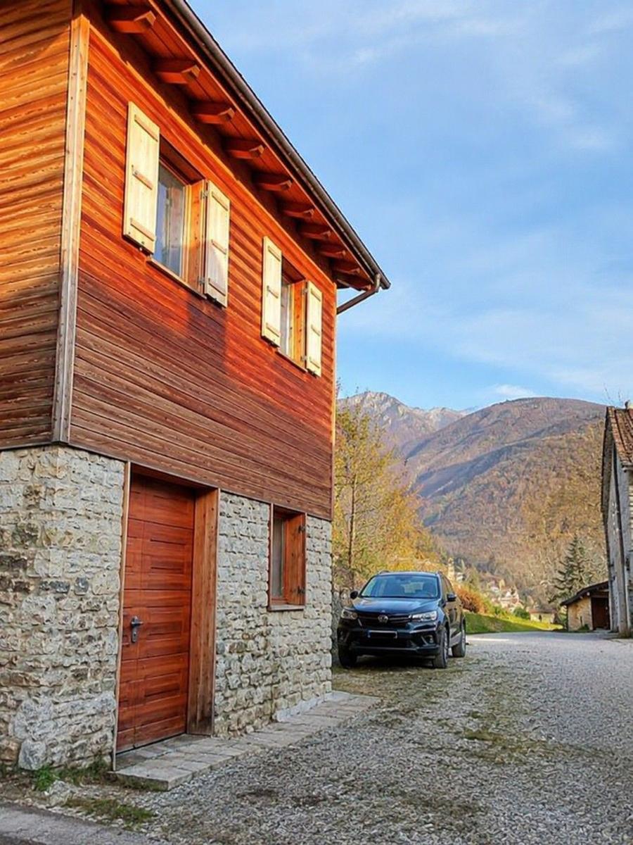 Holzhaus mit Steinsockel, parkende Auto und Berglandschaft im Hintergrund.
