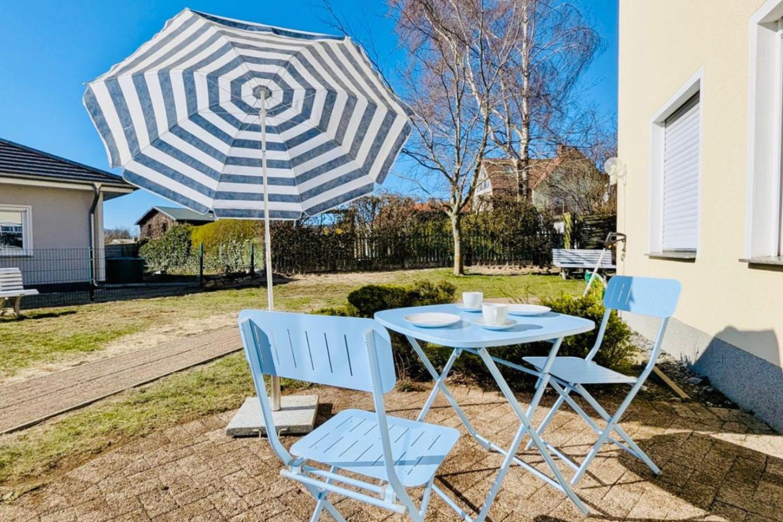Terrasse mit blauem Tisch und Stühlen unter einem gestreiften Sonnenschirm.