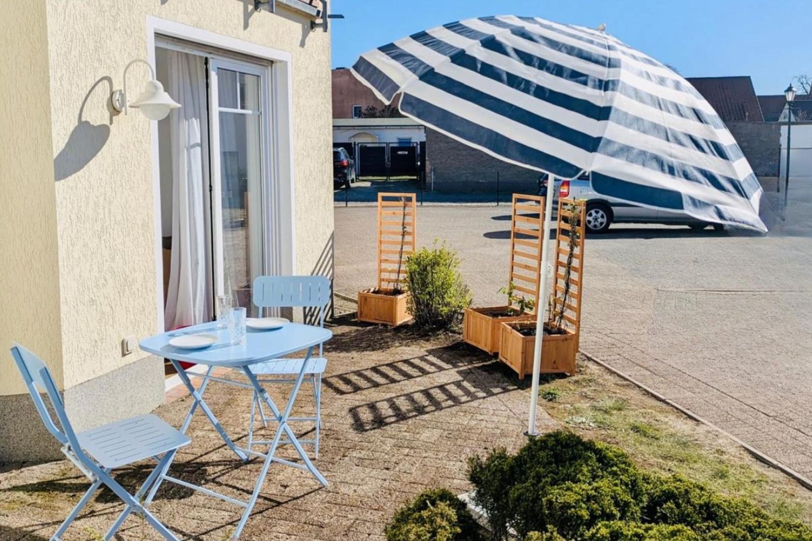 Terrasse mit blauem Tisch, Stühlen und großem gestreiften Sonnenschirm.