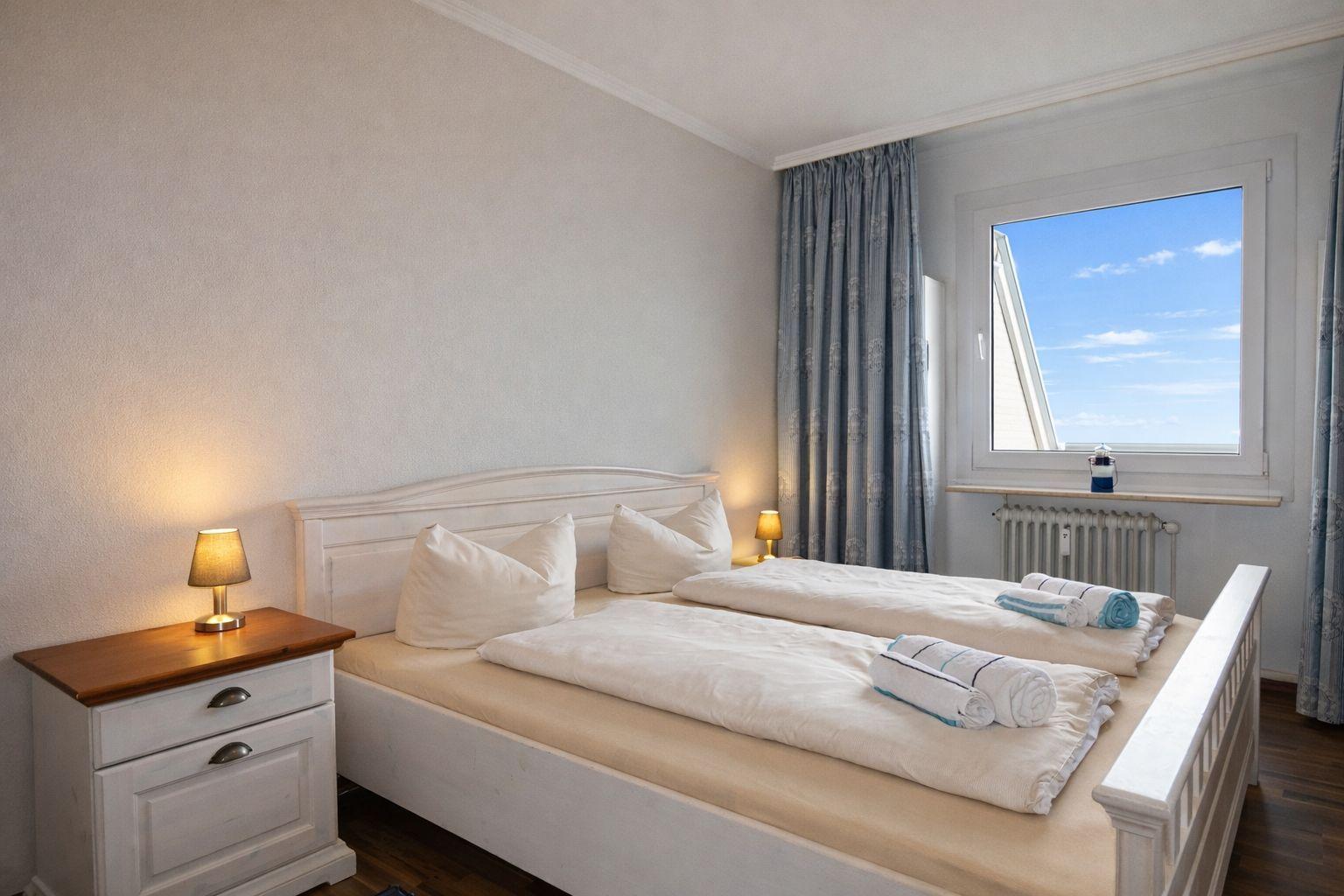 Ein Schlafzimmer mit Doppelbett, Nachttisch und Fenster mit Blick auf den Himmel.