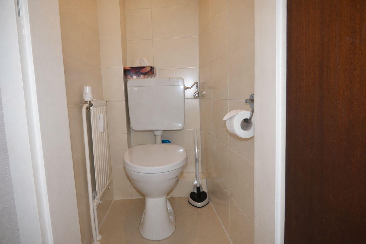 Toilettenbereich mit Toilette, Toilettenpapierhalter und Heizkörper an der Wand.