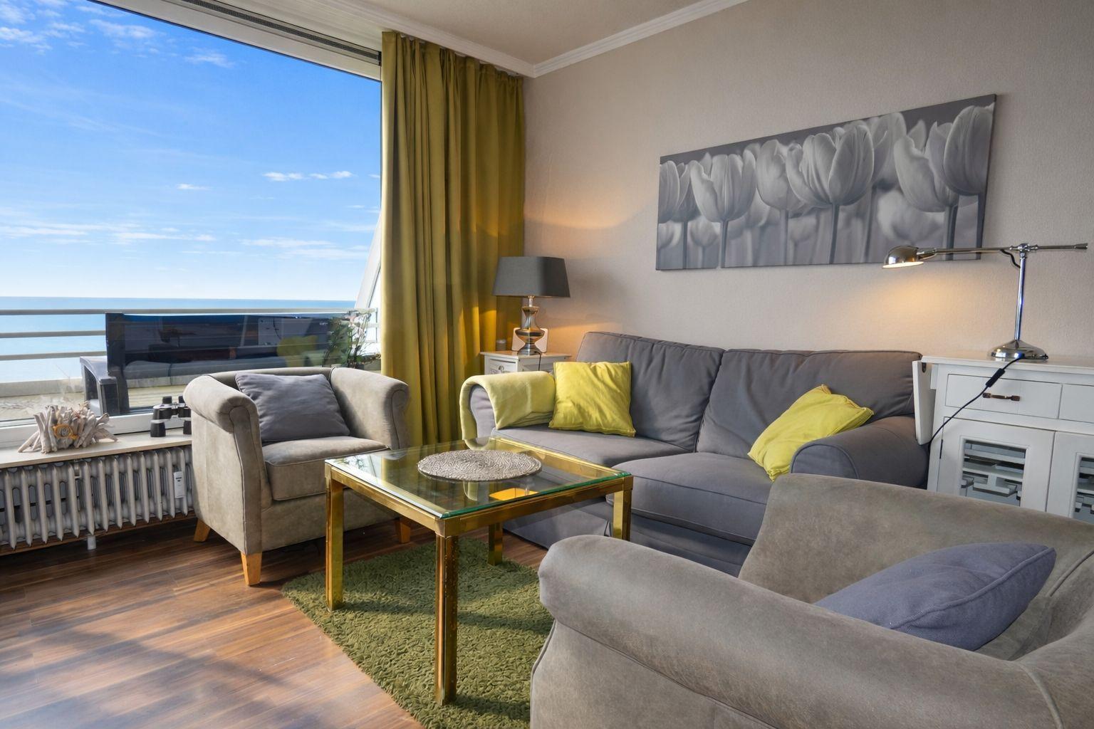Wohnzimmer mit Sofa, Sessel und Glas-Tisch. Blick auf Meer durch großes Fenster.