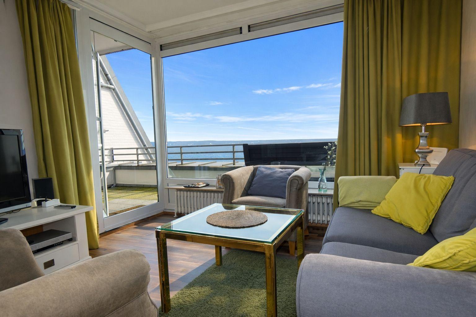 Wohnzimmer mit Meerblick, Sofa, Sessel und Glas-Tisch.