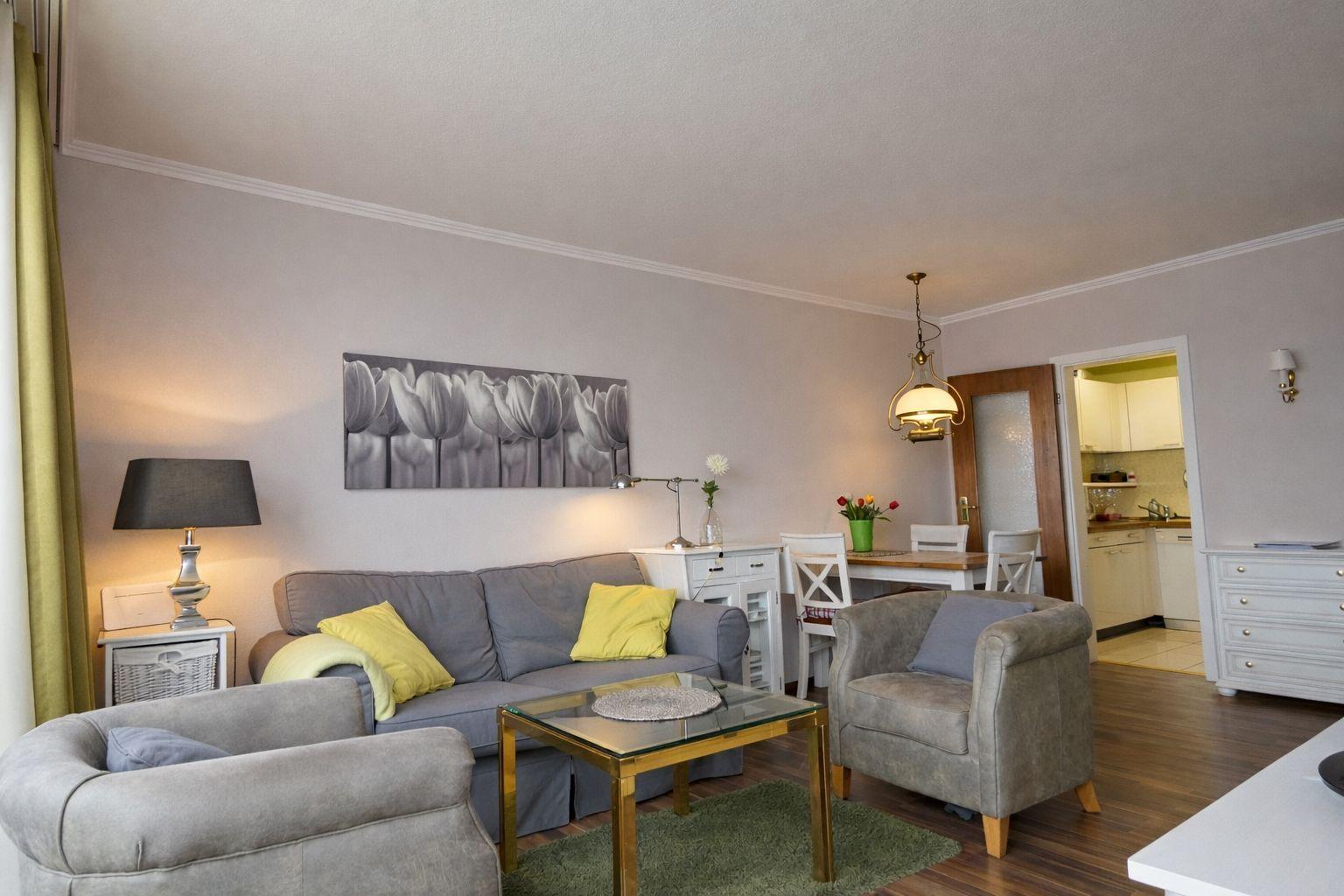 Wohnzimmer mit Sofa, Sesseln und Esstisch. Küche im Hintergrund sichtbar.