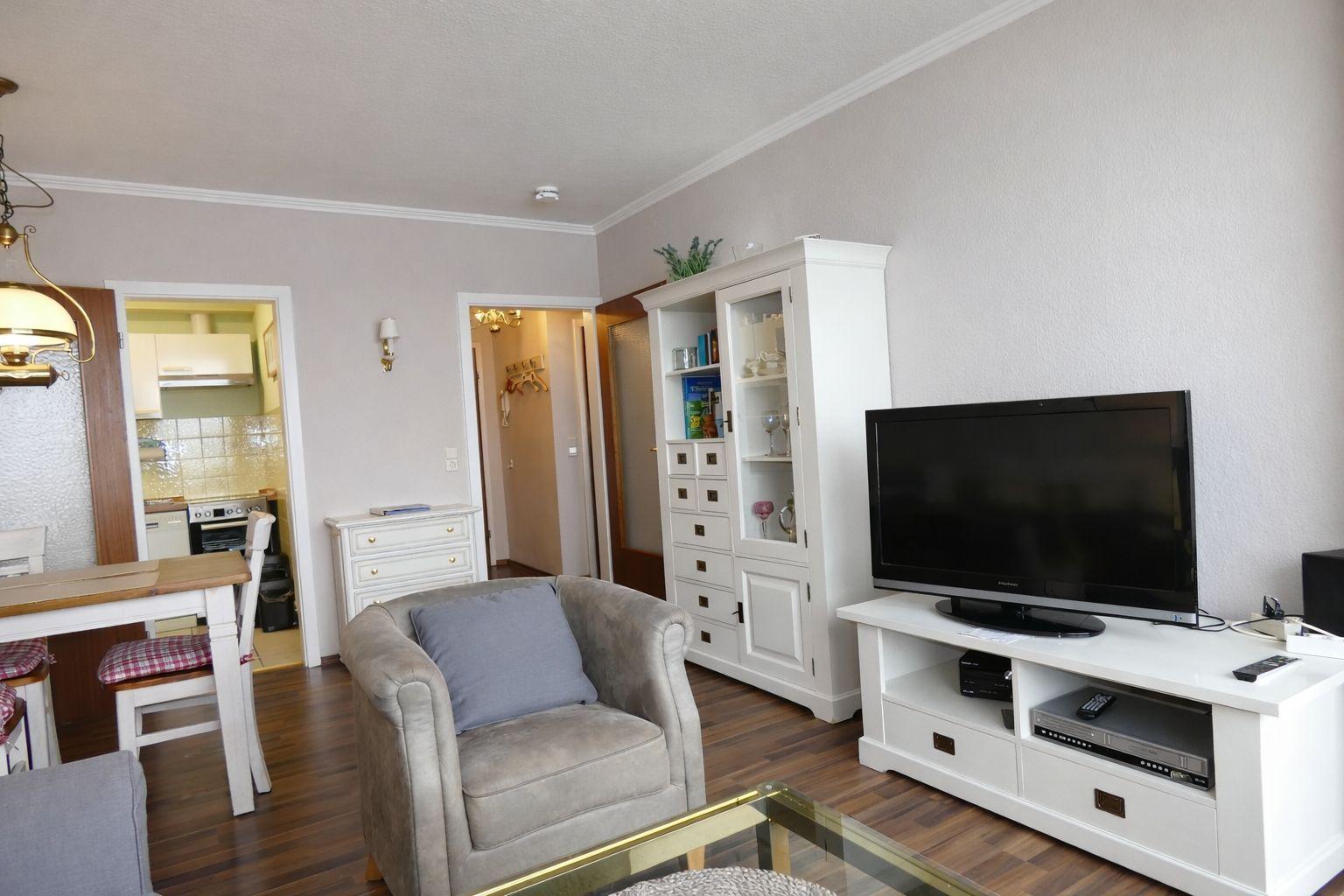 Wohnzimmer mit Fernseher, Sessel und Küchenbereich im Hintergrund.