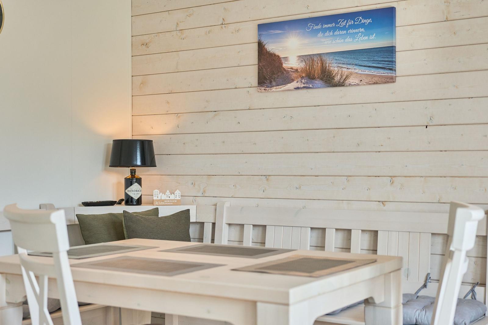 Esszimmer mit Holzwand, Tisch, Stühlen und Wandbild mit Strandmotiv.
