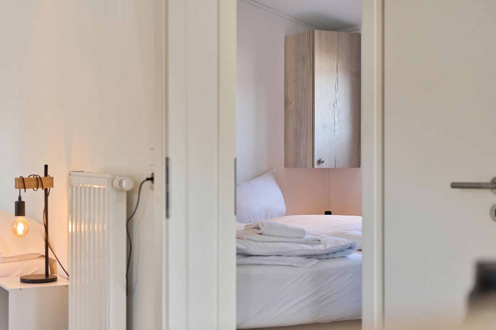 Schlafzimmer mit Bett, Holzschränkchen und Stehlampe.
