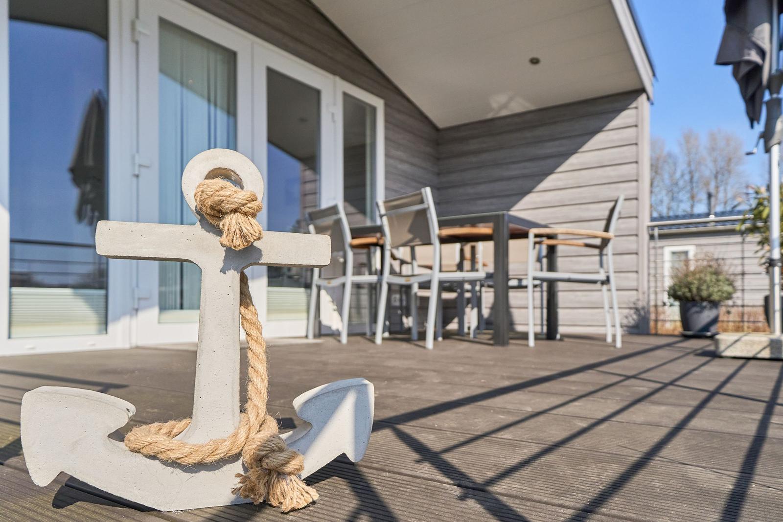 Haus mit Terrasse, Tisch, Stühlen und großer Ankermarke mit Seil.