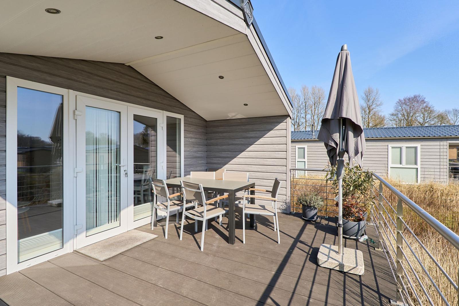Terrasse mit Tisch, Stühlen und Sonnenschirm. Glas-Türen führen ins Innere.