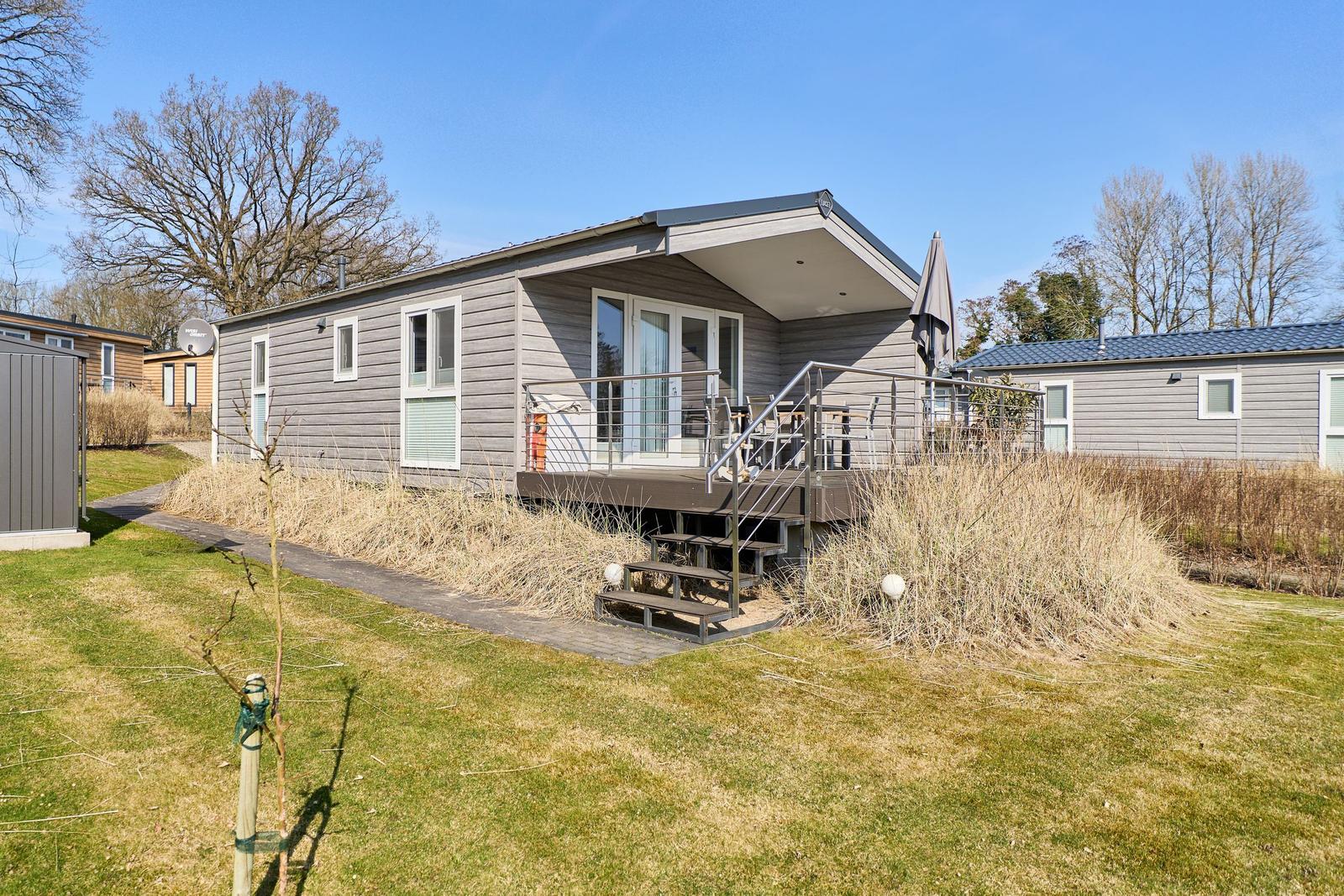 Moderne Ferienhaus mit Terrasse und Garten. Holzverkleidung und Satellitenantenne sichtbar.