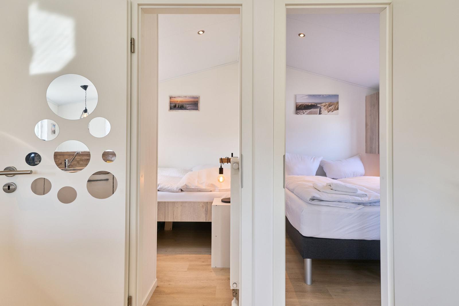 Zwei Schlafzimmer mit Betten und Wandbildern sind über eine Tür mit runden Spiegeln sichtbar.