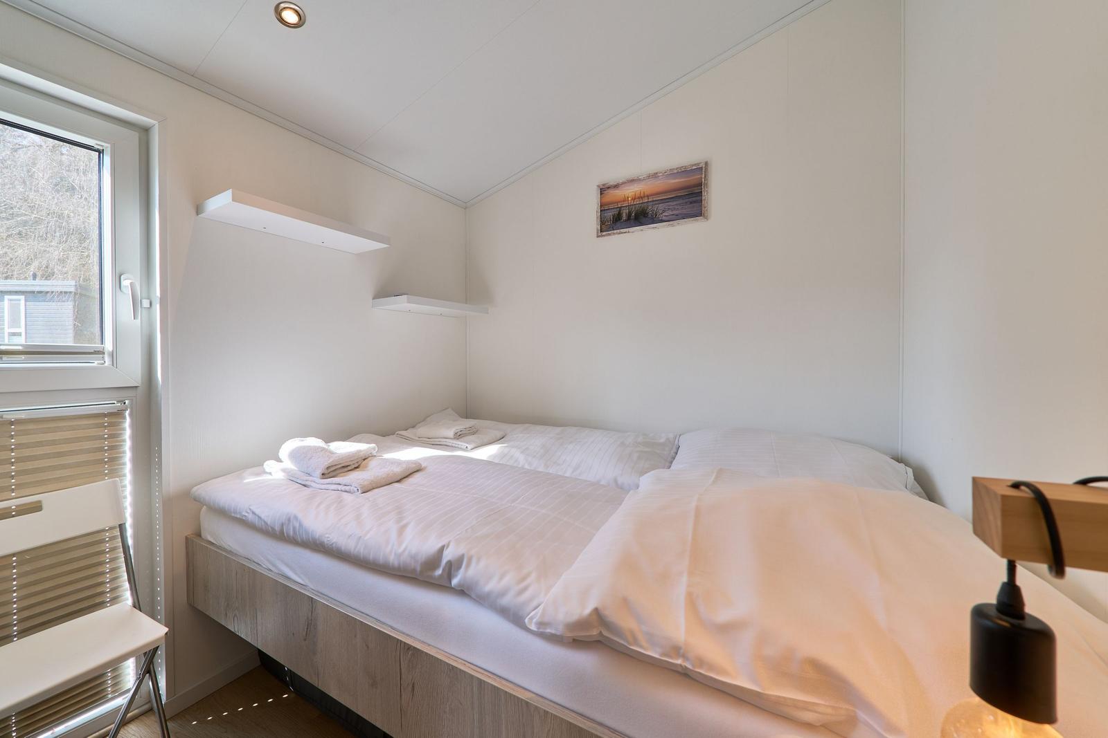 Ein Bett mit weißer Bettwäsche, ein Fenster und eine Wandlampe.