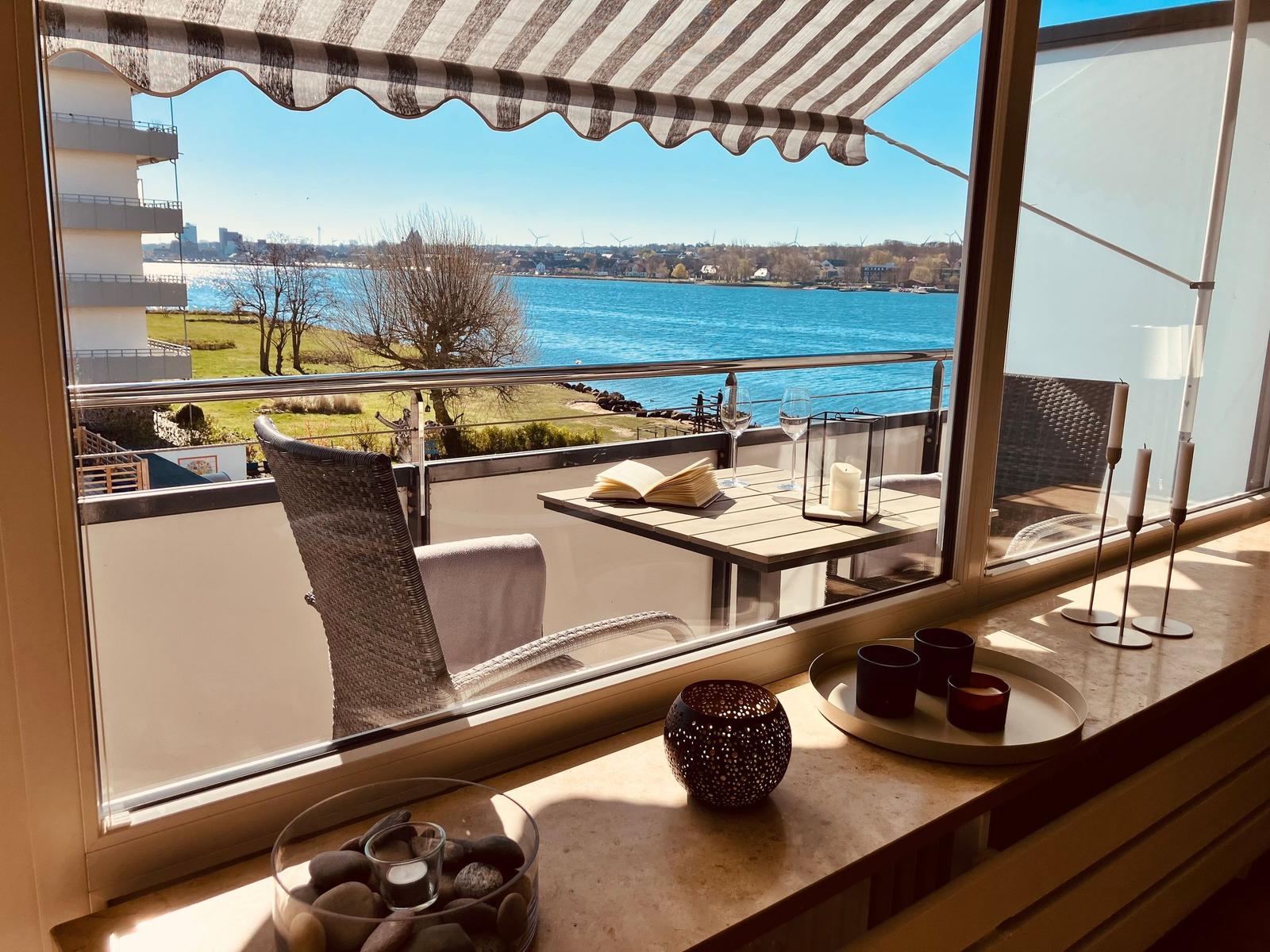 Balkon mit Tisch, Stühlen und Blick auf Wasser und Landschaft.