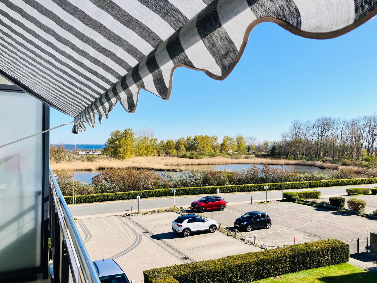 Blick vom Balkon mit Sonnenschutz auf Parkplatz und Flussufer.