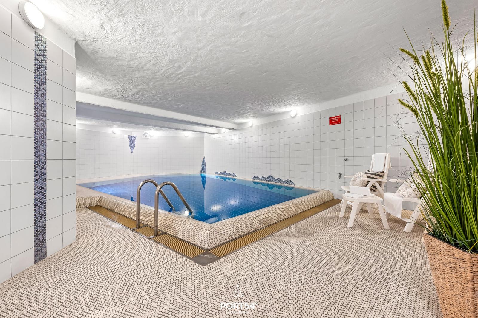 Innere Schwimmhalle mit Pool, Liegestühlen und Pflanze.