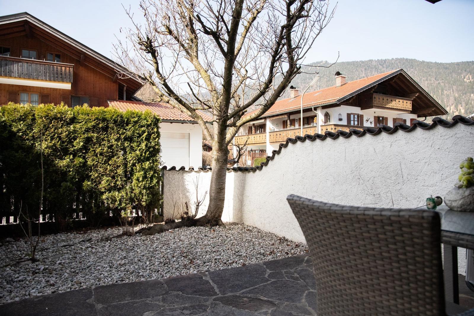 Terrasse mit Steinplatten und Gartenbereich mit Kies, umgeben von weißen Mauern und Bäumen.