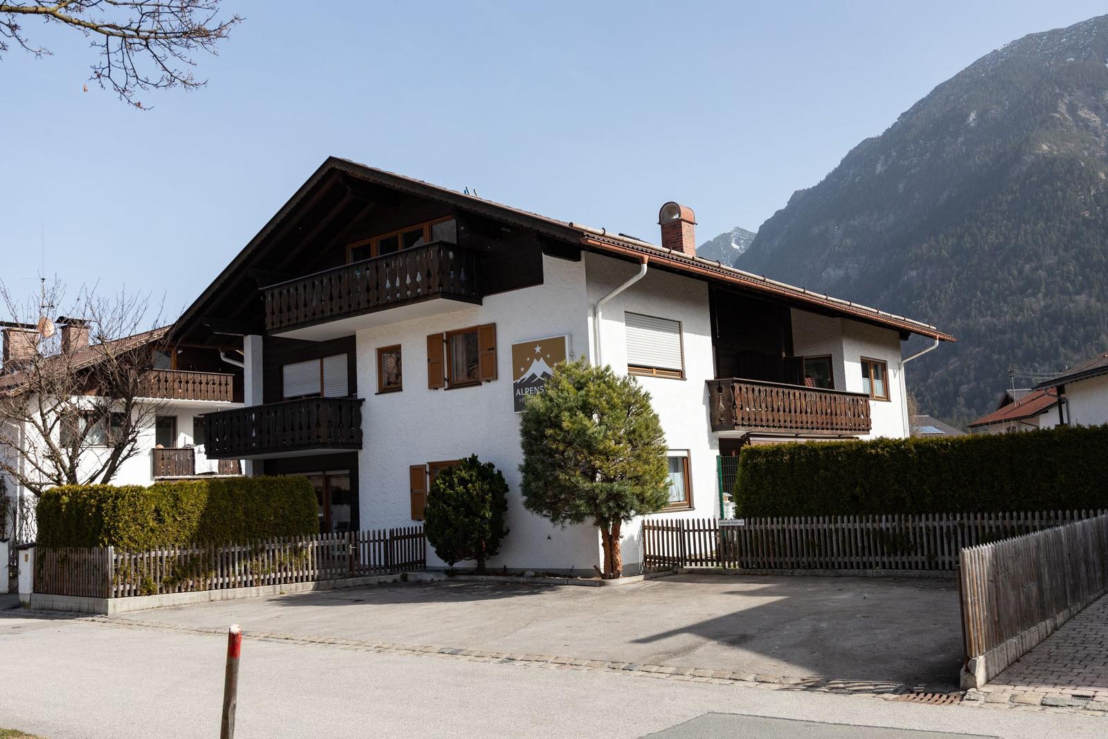 Wohnhaus mit Balkonen und Gartenzaun vor Berglandschaft